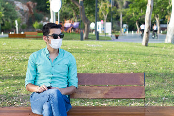 man in medical mask is sitting on a bench on the street during quarantine