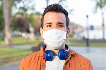 Portrait of young man wearing medical mask posing in sunny park