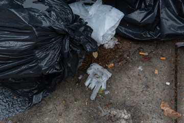 A white latex glove is discarded and laying on the side walk mixed in with bags of trash. This is a common scene as civilians amplify their efforts to protect themselves during a pandemic. - obrazy, fototapety, plakaty