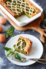 A piece of spinach ricotta pie in front of a whole pie. Close up on the grey background