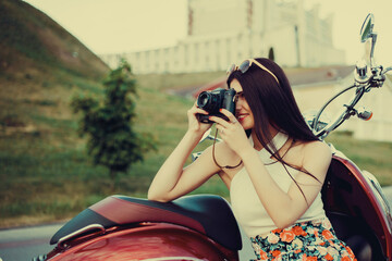 young brunette in a colorful dress and sunglasses in the summer in the city on a scooter with a...