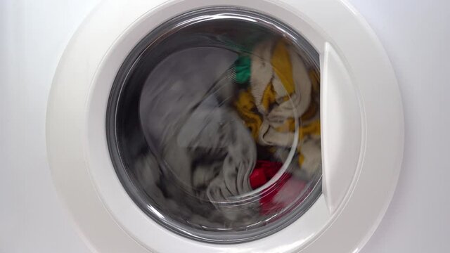 Washing machine with dirty clothes inside. Front view ashing things in the washing machine. Rtation of the drum of the washing machine. Close-up front cover of household equipment