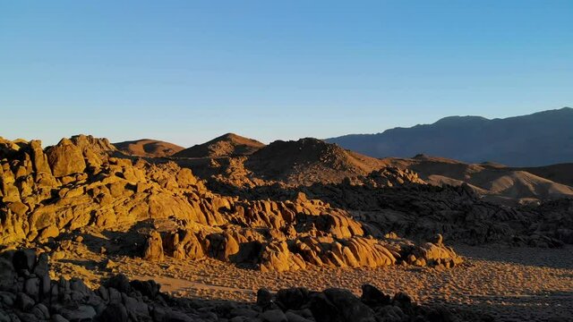 Aerial flyover through rugged boulders by alpine mountains in morning light at Alabama Hills, Eastern Sierra
