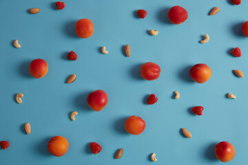 Set of ripe peaches, raspberry, cashew and almond nuts on blue background. Ingredients for tasty quick snack or preparing breakfast. Healthy source of vitamins. Vegetarian food. Selective focus