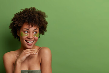 Good looking cheerful woman keeps hand gently under chin, looks thoughtfully aside, wears hydrogel...