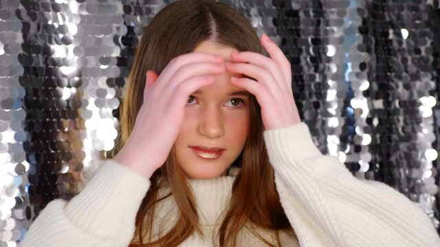 Close up teenager girl model with beautiful make-up smiles and poses for the photographer at the camera on a shiny silver background in a beauty salon. 4K slow motion footage