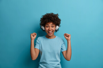People, happiness, hobby concept. Joyful African American woman listens favorite audio track,...