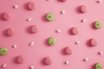 Colorful macaroon french cakes with pistachio and strawberry natural flavor, creamy stuffing, white marshmallow around. Yummy traditional homemade cookies. Flat lay on pink background. Sweet snack