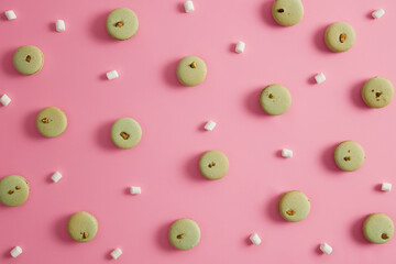 Round green french macaroons of pistachio flavor, marshmallow on pink background. Yummy nourishing sweet dessert. Food photo. High calories cookies. Confectionery, bakery concept. Seamless pattern