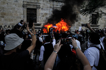 Un grupo de manifestantes tomando fotos y videos de una patrulla en llamas.