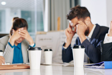 Cups of take out coffee on table in front of business people meeting to discuss economic consequences of covid-19 pandemic