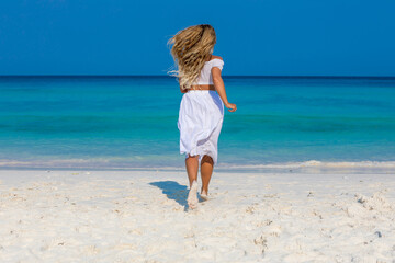 Young beautiful girl in white clothes walks along the sandy beach near the water