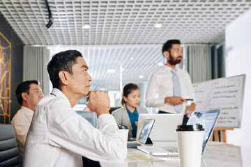 Frowning serious Asian entrepreneur attending business meeting and watching presentation on new anti crisis measures