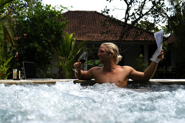 young man sitting in jacuzzi, drinking wine and reading document
