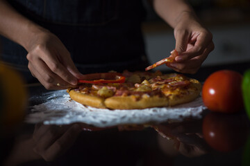 close-up of human hands in the apron knead the dough on a black wooden table, sprinkle with flour.Making dough by hands at bakery.