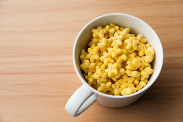 Yellow star shaped honey coated cereal inside a mug on a wooden table.
