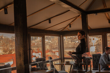 Female posing in cafe  on the roof of the city and using a laptop.  Fashion woman dressed style black  golf and shorts. Freelancer relexing on the rooftop and holding computer.