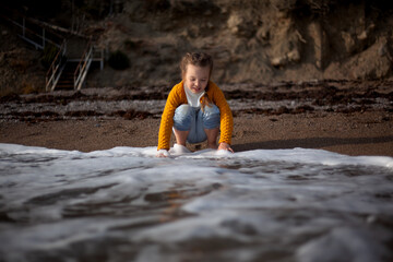 Female kid playing with water in the beach against stone. Barefoot child runs on the sand st the shore of sea in the nature . Happy leisure have fun vacation