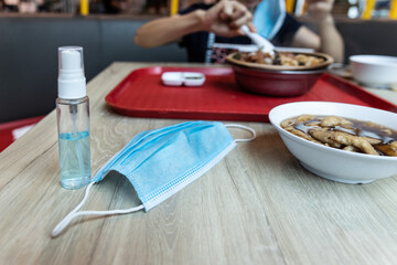 Fototapeta na wymiar Face mask and sanitizer on table next to meal, new normal post coronavirus pandamic.