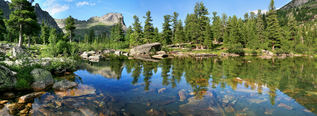 Wild forest lake in the Sayan Mountains, Natural Park Ergaki. Siberian nature, traveling in Russia. Wide panoramic view.