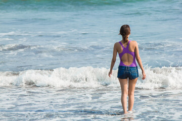 young woman in purple bikini walking among the waves
