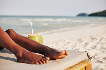 Cropped image of young Black woman resting on chaise-lounge and drinking refreshing coconut water...
