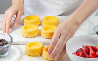 Biscuit cakes with fresh berries, chocolate, and whipped heavy cream. Woman preparing dessert, mini biscuit cups with strawberries and blueberries,  close up on white background