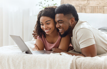 Black couple in love surfing internet together, lying on bed