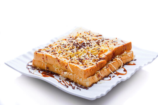 Toast on a plate. Burnt bread sprinkled with chocolate sprinkles, grated cheese, and sweetened condensed milk. Isolated on a white background.