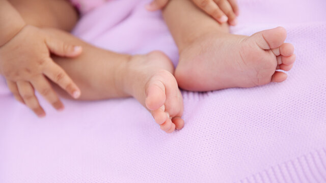 Baby girl sitting on pink blanket with barefeet, closeup of tiny feet