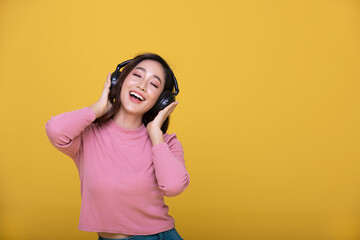 Happy cheerful Beautiful Asian woman wearing wireless headphones enjoying listening to music on yellow background.People lifestyle concept