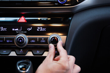Hand turning on car's air conditioner dial. Hand adjusting heater temperature button.