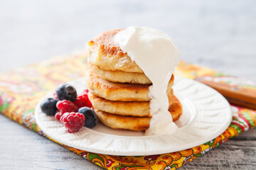 Summer cottage cheese pancakes on white plates on a  table with sour cream and berry, closeup, selective focus