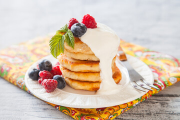 Summer cottage cheese pancakes on white plates on a  table with sour cream and berry, closeup, selective focus