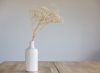 A white ceramic bottle with a dry flower stands on a wooden surface.