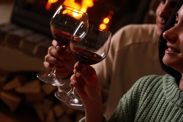 Lovely couple with glasses of wine near fireplace indoors, closeup. Winter vacation