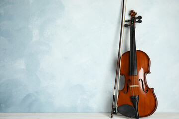 Beautiful violin and bow on white wooden table near light blue wall. Space for text
