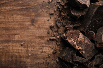 Pieces of dark chocolate on wooden table, flat lay. Space for text