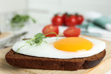 Tasty fried chicken egg with sprouts and rye bread on wooden board, closeup