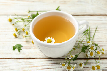 Cup of tea and chamomile flowers on white wooden table