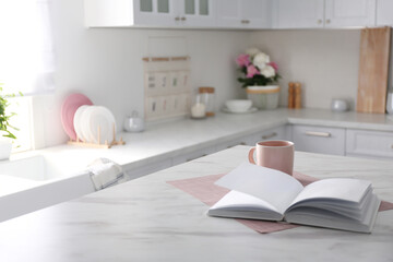 Book and cup on white marble table in modern kitchen. Interior design