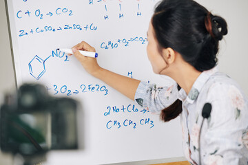 Chemistry teacher recording herself drawing chemical element structure on whiteboard