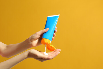 Woman applying sun protection cream on hand against yellow background, closeup. Space for text