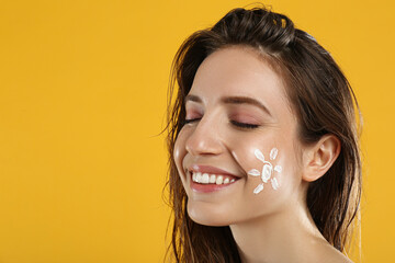 Young woman with sun protection cream on face against yellow background. Space for text