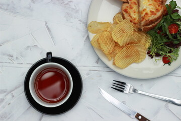 Quesadilla bread on a plate with healthy vegetables, crackers, fork-knives and a cup of tea in a glass. Top view