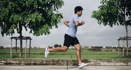 Side view of young asian man running outdoors in park