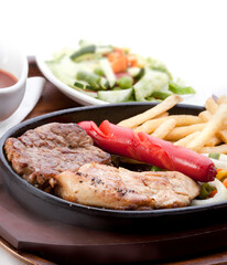 Chicken breast steak, beef steak, fried sausages, french fries, served on a hot plate, with pickles and barbecue sauce.