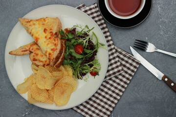 Quesadilla bread on a plate with healthy vegetables, crackers, fork-knives and a cup of tea in a glass. Top view