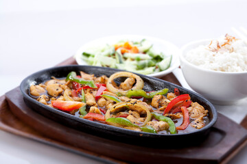 The chicken with yakiniku sauce cooked with green chili, paprika, and onion, sprinkled with sesame seeds. Served on a hot plate with a bowl of white rice and pickles.