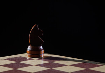 Wooden chess piece horse alone on a board with black background looking to the right